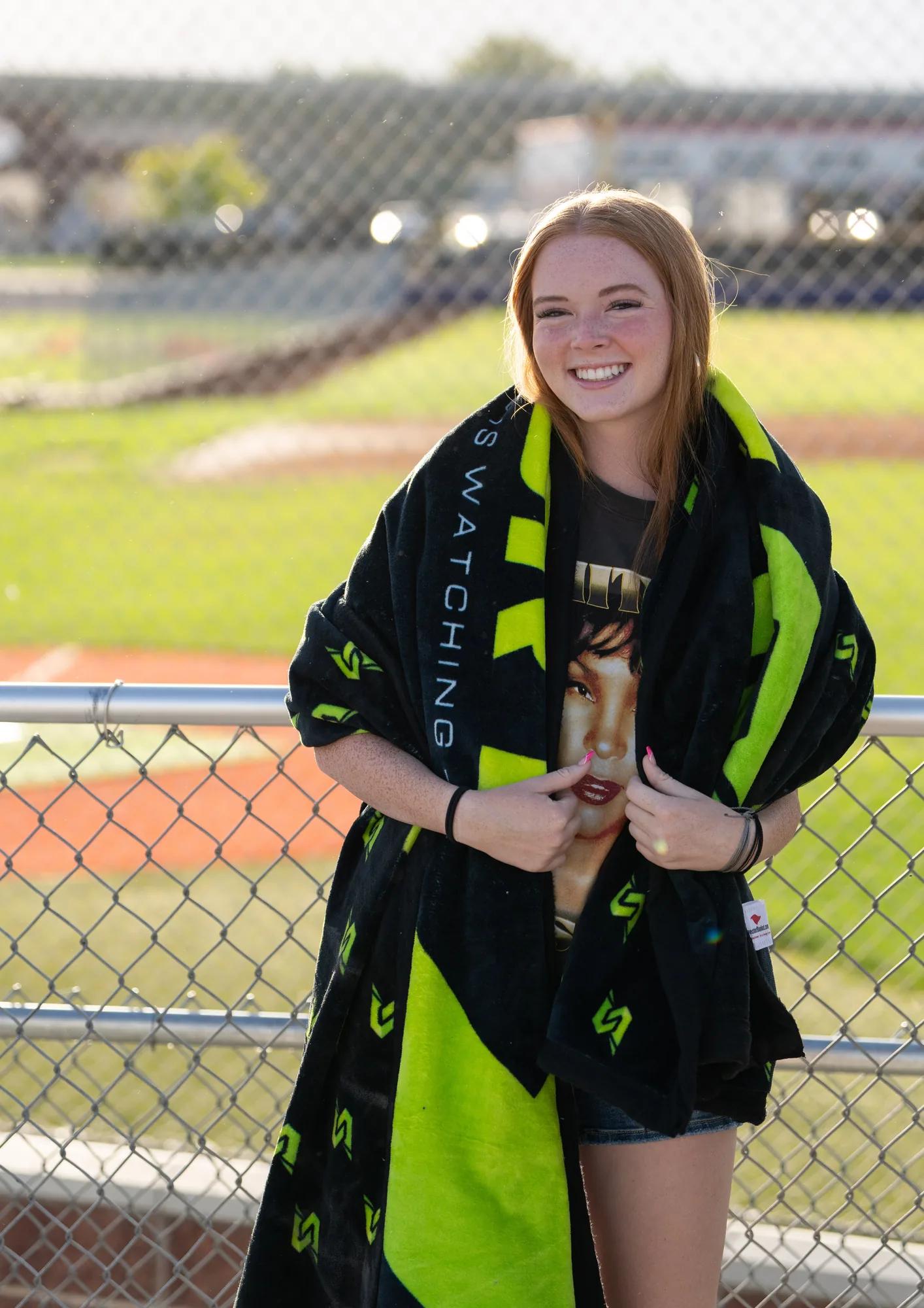 A student wrapped warm in a custom blanket at a field at golden hour